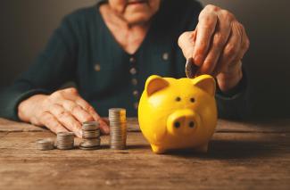 Elderly hands depositing coins into a yellow piggy bank. by Sasun Bughdaryan courtesy of Unsplash.
