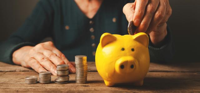 Elderly hands depositing coins into a yellow piggy bank. by Sasun Bughdaryan courtesy of Unsplash.